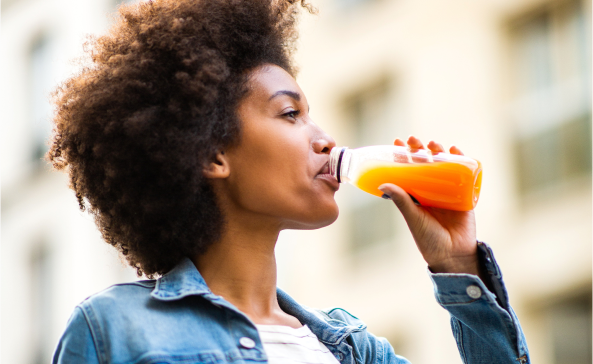 A woman standing outside drinking a reduced sugar fruit drink from the bottle.