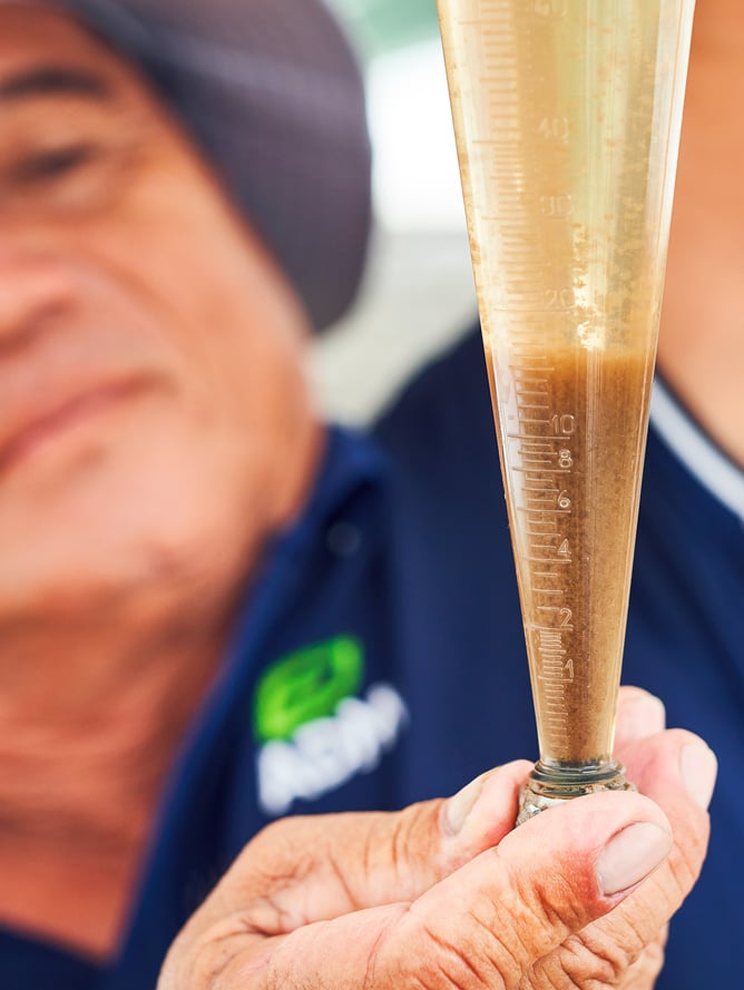 A male scientist is holding a sample of blown fluid containing ingredients for aquaculture.