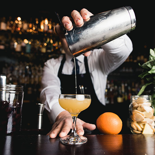 A bartender pouring a sophisticated alcoholic drink in a dark setting room