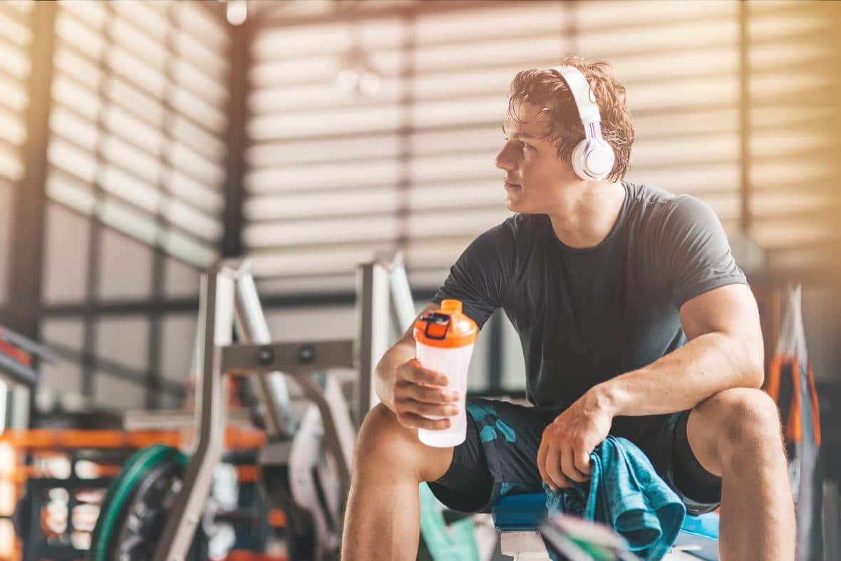 An athletic man in headphones listening to music and holding a pre-workout drink