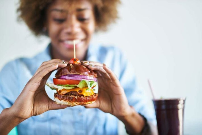 smiling african woman about to eat a meatless vegan cheese burger