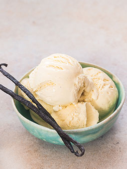 A bowl of vanilla ice cream next to vanilla beans