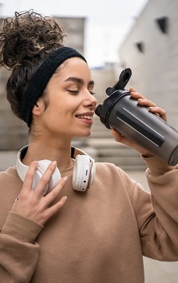 A woman in gym outfit is drinking dietary supplements