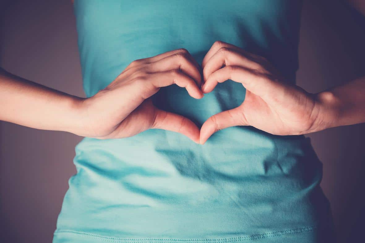 A woman making a heart symbol over her stomach