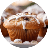 A close-up of a single blueberry muffin covered in powdered sugar and a light drizzle of icing among a tray of the muffins.