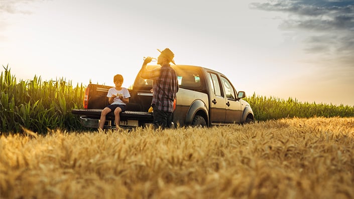 C30 Father and child relaxing in pickup truck bed outside corn field