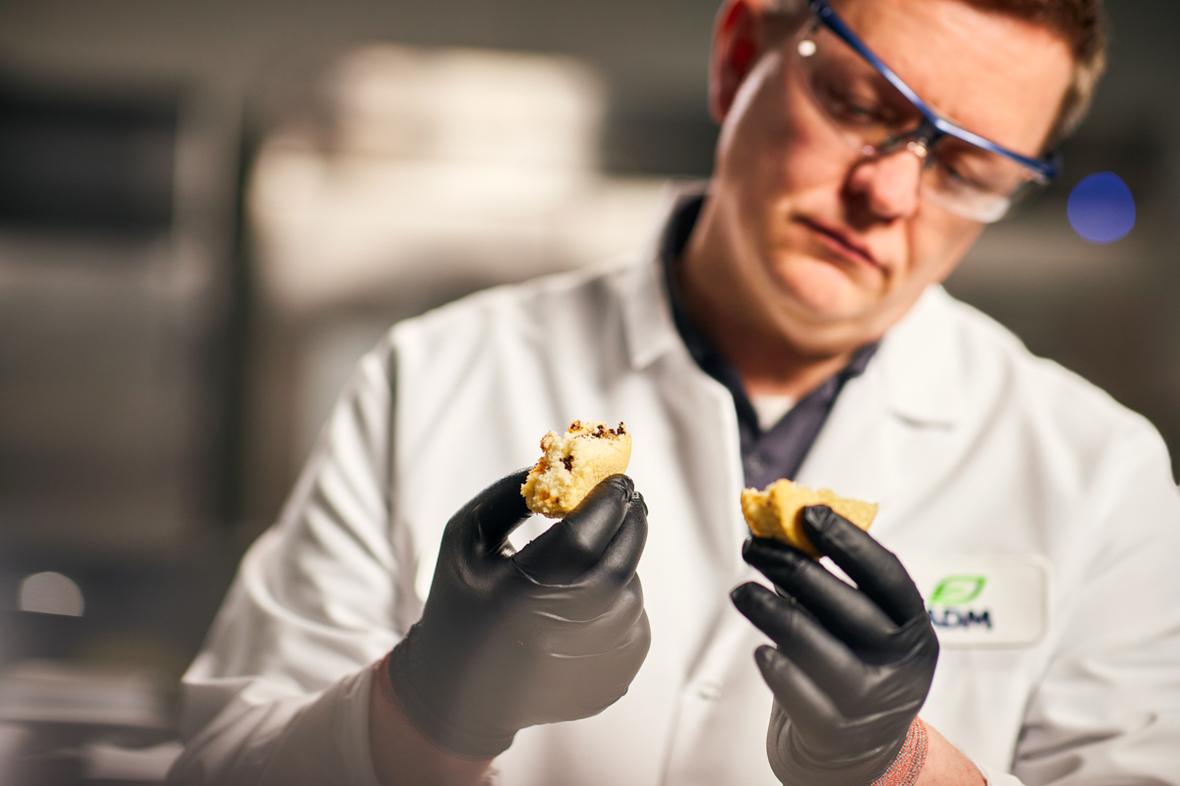 Scientist wearing white ADM lab coat and safety equipment breaking apart and analyzing a muffin